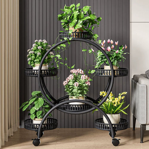 A white metal plant stand with six trays, each holding a potted plant, positioned on a floor with a dark grey wall in the background.